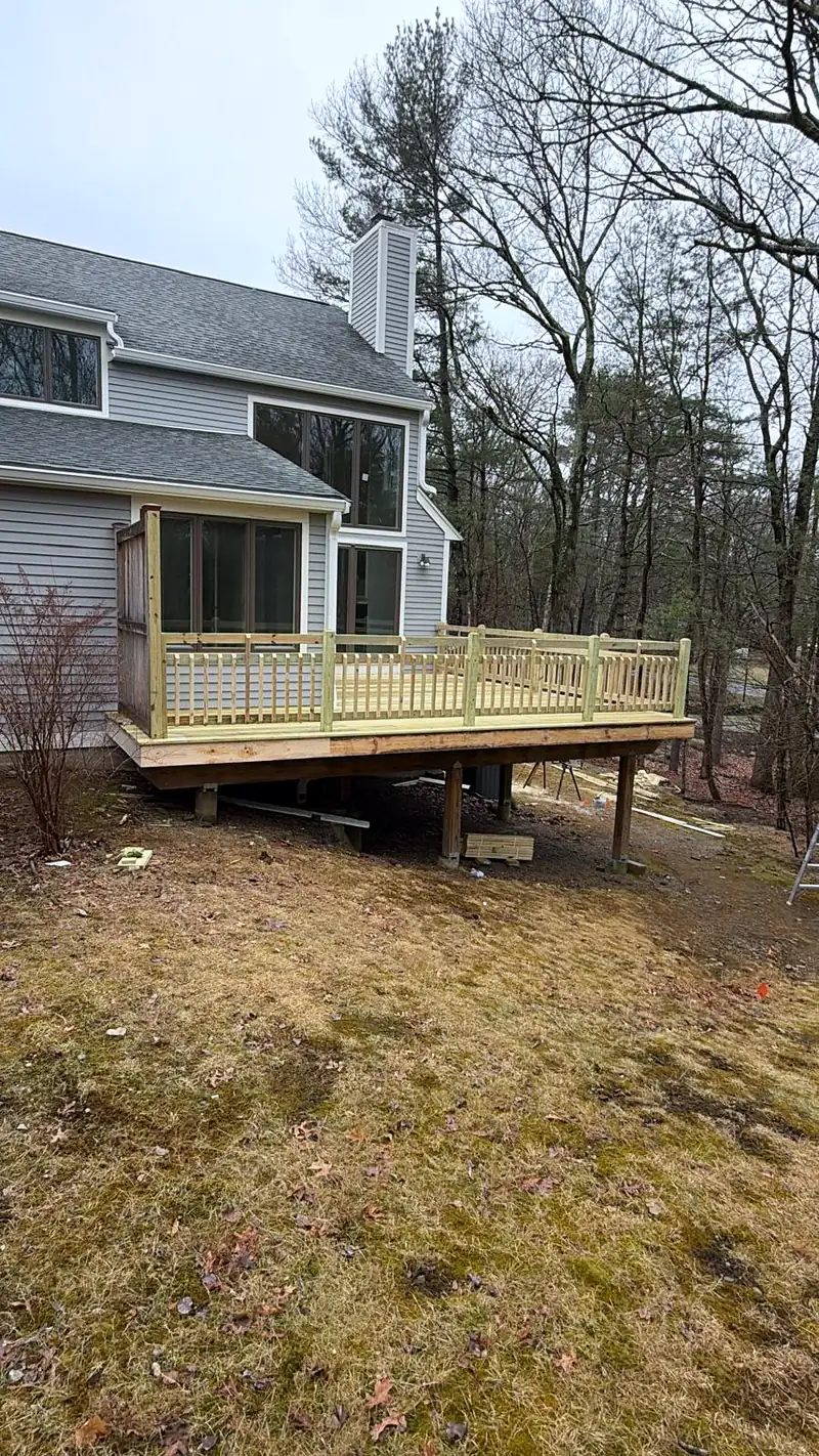 New elevated wood deck with railing on the back of a gray house