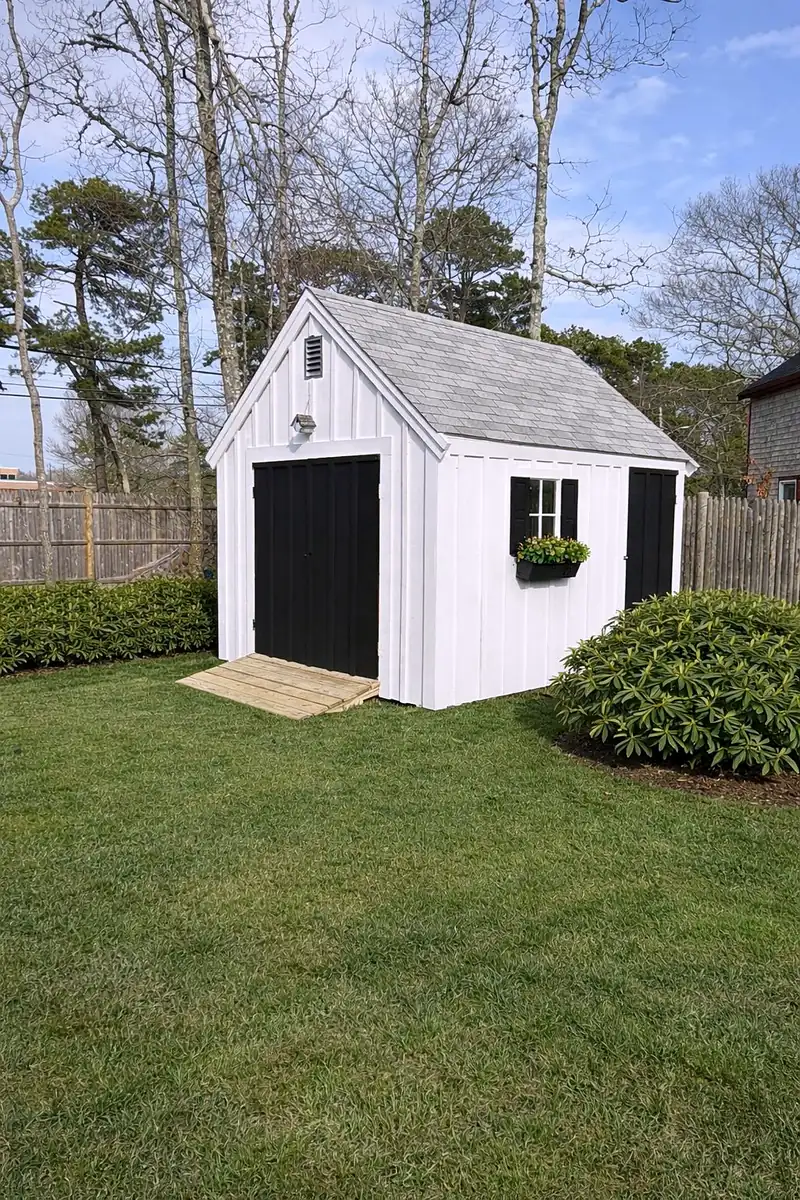 Restored white garden shed with black doors and shutters on a green lawn